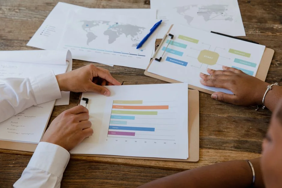 Mains tenant un smartphone à côté d’un ordinateur portable avec des graphiques boursiers, illustrant le trading numérique.